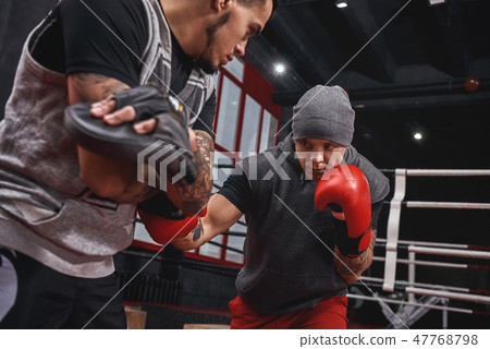Close quarter boxing. Strong tattooed athlete in sports clothing training on boxing paws with 47768798