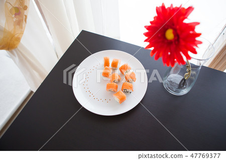 Sushi roll with salmon, philadelphia on a white plate. Red flower in a vase. Sushi roll with salmon, philadelphia on a white plate. Red flower in a vase. 47769377