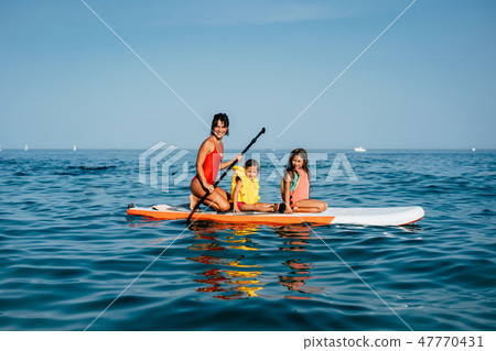 Mother with two daughters stand up on a paddle board Mother with two daughters stand up on a paddle board 47770431