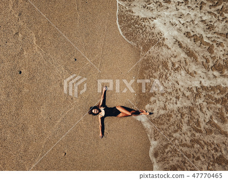 Aerial top view young woman lying on the sand beach and waves Aerial top view young woman lying on the sand beach and waves 47770465