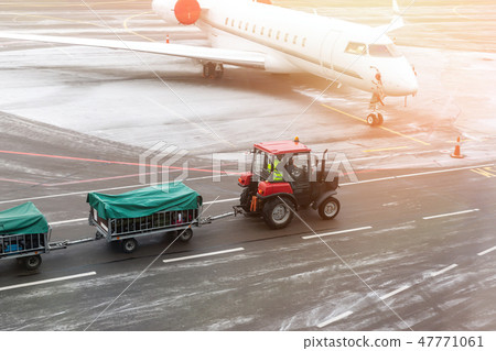 cargo freight tractor machine delivering luggage carts to airplane at airport. Airport carrier and 47771061