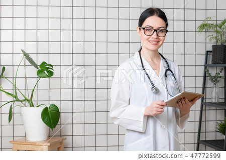 Beautiful smiling doctor wearinbg glasses standing in her modern office Beautiful smiling doctor wearinbg glasses standing in her modern office 47772599
