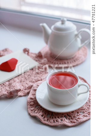Cup of scented pink tea on crocheting napkin Cup of scented pink tea on crocheting napkin 47781221
