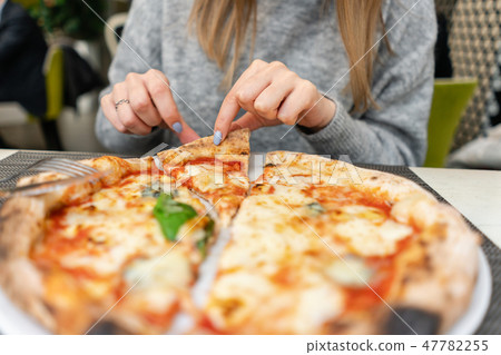 A woman is eating Neapolitan pizza from wood-burning stove. lunch in an Italian restaurant. Table 47782255