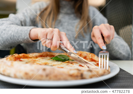 Woman eats with knife and fork a pizza Margherita with mozzarella tomatoes and basil. Neapolitan 47782278