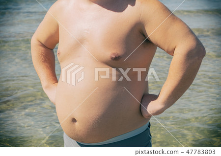 A fat man in shorts stands on the shore of the sea A fat man in shorts stands on the shore of the sea 47783803