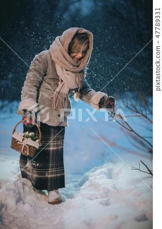 little girl with basket goes and looks for the first flowers under the snow in forest in winter 47789331