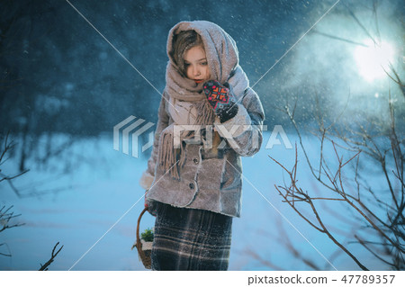 little girl with basket goes and looks for the first flowers under the snow in forest in winter 47789357