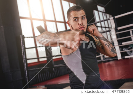 Great hook. Muscular athlete in sports clothing throwing hook punch opposite boxing ring 47789865