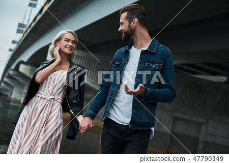 Romantic date outdoors. Young couple walking on the city street holding hands talking smiling joyful 47790349