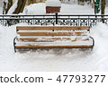a snowy wooden bench and metal hedge behind  47793277