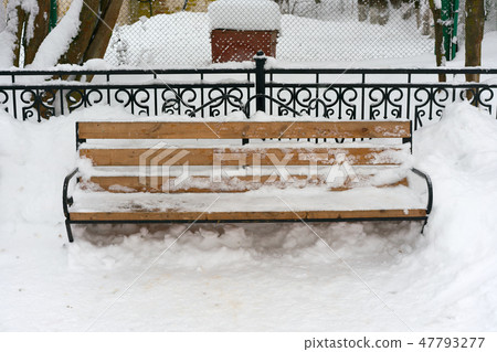 a snowy wooden bench and metal hedge behind a snowy wooden bench and metal hedge behind 47793277