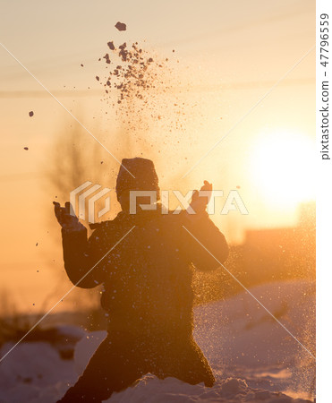A boy throws snow into the sky at sunset A boy throws snow into the sky at sunset 47796559
