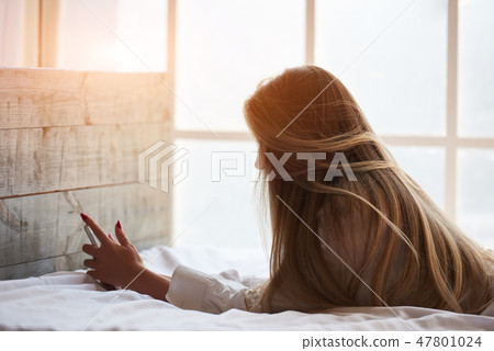 Woman in bed holding phone. 47801024