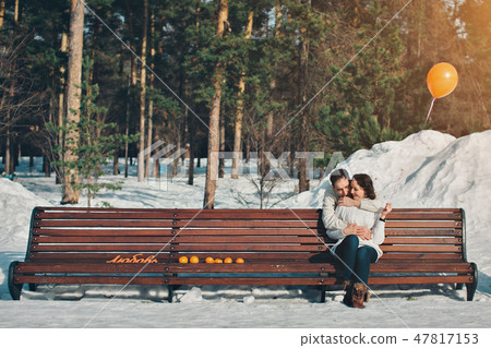 Valentine's day: a couple in love sitting on a bench in a winter forest with an orange balloon and Valentine's day: a couple in love sitting on a bench in a winter forest with an orange balloon and 47817153