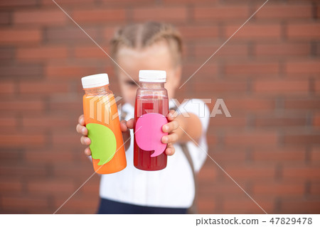 A girl holds in her hands healthy carrot juice to drink . Close-up of a orange glass bottle. Trend 47829478