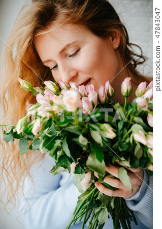 Portrait of a young beautiful girl with a bouquet of roses near window.  47843047