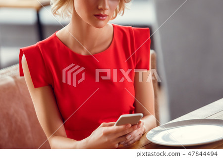 Young woman on date in restaurant sitting chatting with boyfriend on smartphone serious close-up 47844494