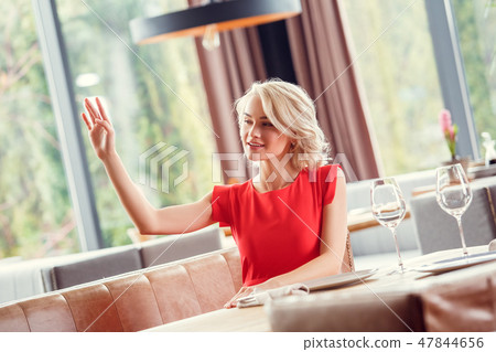 Young woman dining in restaurant sitting waving to waiter cheerful 47844656