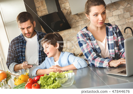 Family at home standing in kitchen together father and son playing game on digital tablet while Family at home standing in kitchen together father and son playing game on digital tablet while 47844676