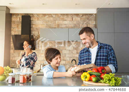 Family at home in kitchen together father and son standing looking at eggs laughing playful while 47844688