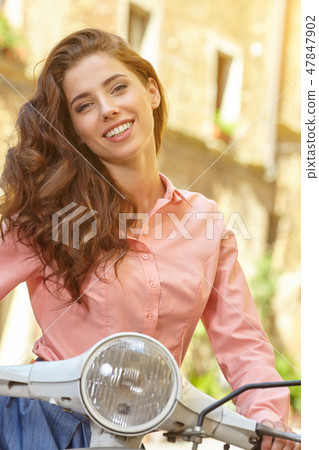 Young beautiful italian woman sitting on a vintage scooter. 47847902