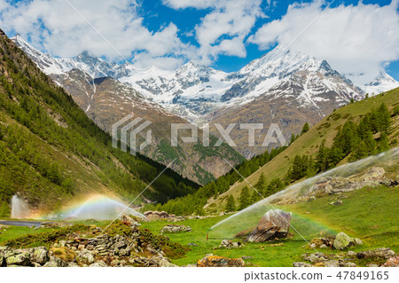 Rainbows in irrigation water spouts, Alps mountain 47849165