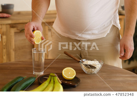 overweight man squeezing lemon juice into water 47852348