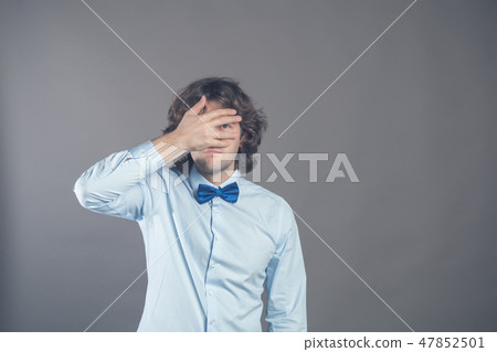 Horizontal shot of unshaven caucasian young curly male covers eyes with palm, tries to be hidden Horizontal shot of unshaven caucasian young curly male covers eyes with palm, tries to be hidden 47852501