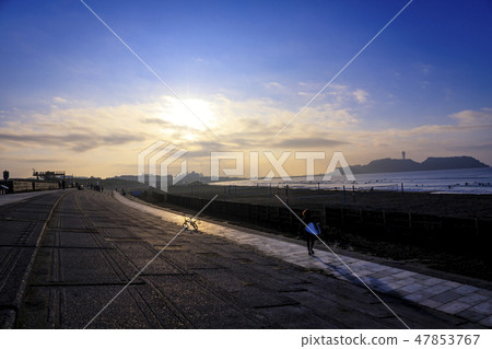 A surfer heading to the sea where Enoshima can be seen under the light shining rising sun 47853767