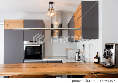 Modern kitchen interior with lights on. Brown wooden table and bar stools, coffee machine 47865397