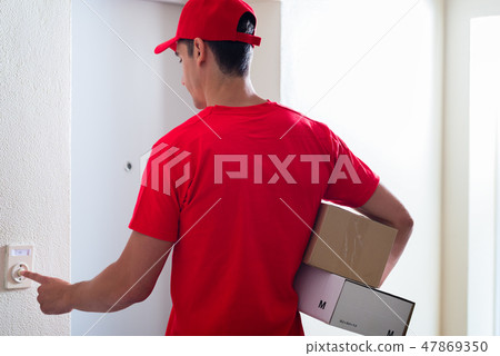 Courier man carrying cardboard boxes ringing the doorbell 47869350