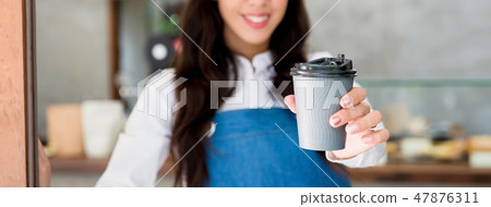 Young female cafe staff giving takeaway coffee cup 47876311