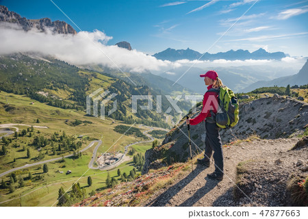 Active hiker hiking, enjoying the view, looking at Dolomites mountains landscape 47877663