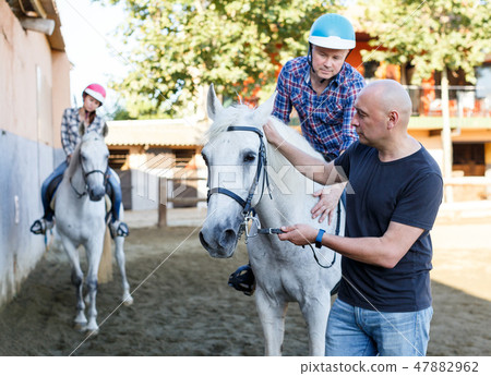 Mature couple with trainer riding horse at farm outdoor 47882962