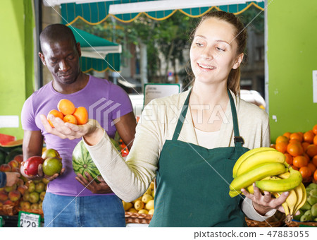 Seller woman is helping man choose exotic fruits 47883055