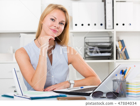 portrait of woman sitting at workplace and smiling in office 47884034