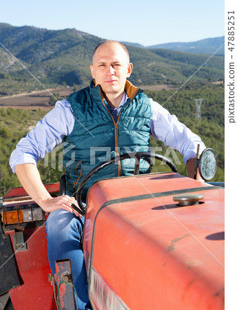 Confident male owner of vineyard driving tractor outdoors in sunny day 47885251