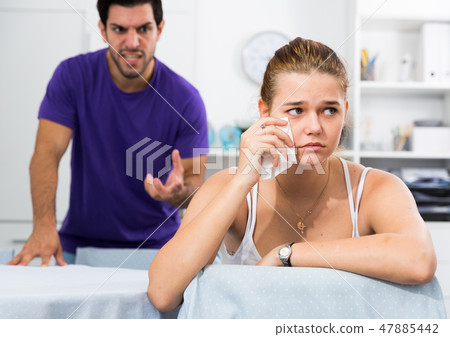 Stressed woman at table with screaming husband behind Stressed woman at table with screaming husband behind 47885442