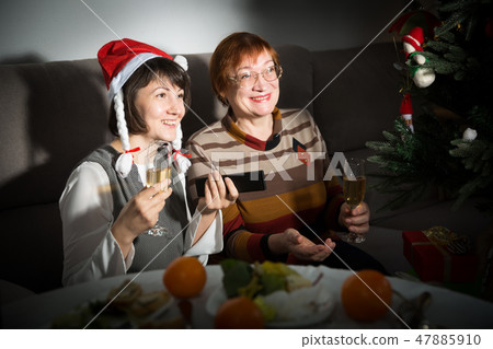 Happy mother and daughter drink champagne and watch TV on Christmas night 47885910