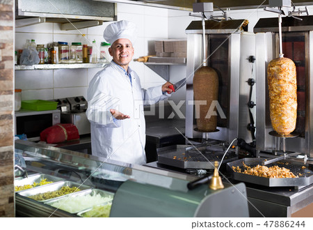 man chef wearing uniform cutting meat for kebab on kitchen in fast food restaurant man chef wearing uniform cutting meat for kebab on kitchen in fast food restaurant 47886244