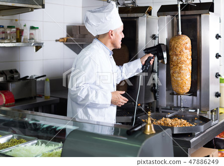man chef wearing uniform cutting meat for kebab on kitchen in fast food restaurant man chef wearing uniform cutting meat for kebab on kitchen in fast food restaurant 47886249