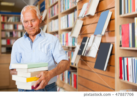 Portrait of intelligent older man in library with pile of books in hands 47887706