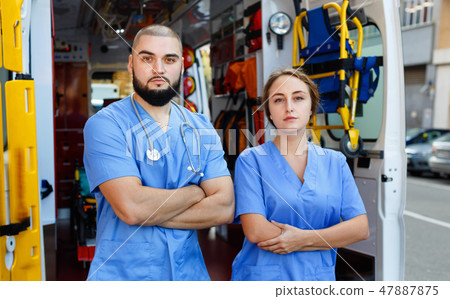 Two confident paramedicals in uniform posing near ambulance car 47887875
