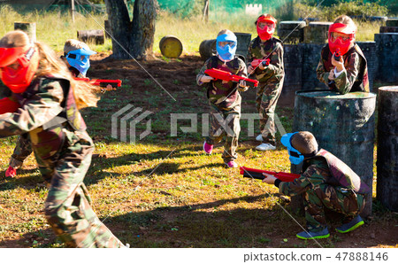 Children paintball players of opposite teams playing in shootout outdoors Children paintball players of opposite teams playing in shootout outdoors 47888146