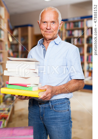 Portrait of happy intelligent older man in library with pile of books in hands Portrait of happy intelligent older man in library with pile of books in hands 47888152