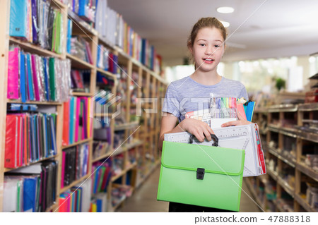Cute tweenager girl holding stack of school stationery in shop 47888318