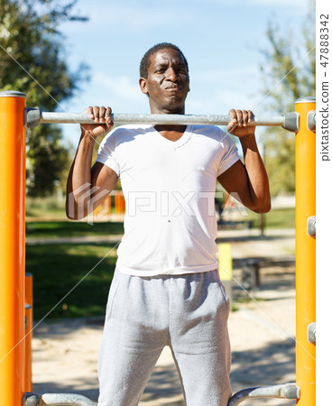 Active african american man doing workout at pull-up bar in park Active african american man doing workout at pull-up bar in park 47888342