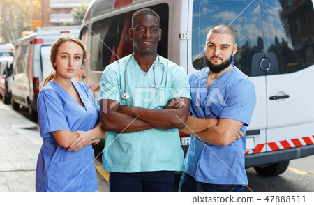 Portrait of ambulance team of three standing near ambulance car 47888511