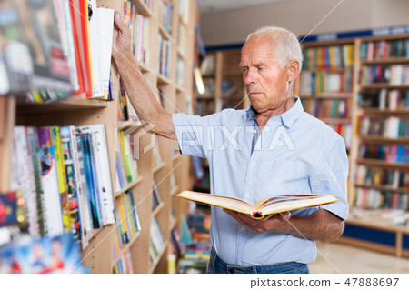 Senior male interested in books looking for necessary literature on shelves Senior male interested in books looking for necessary literature on shelves 47888697